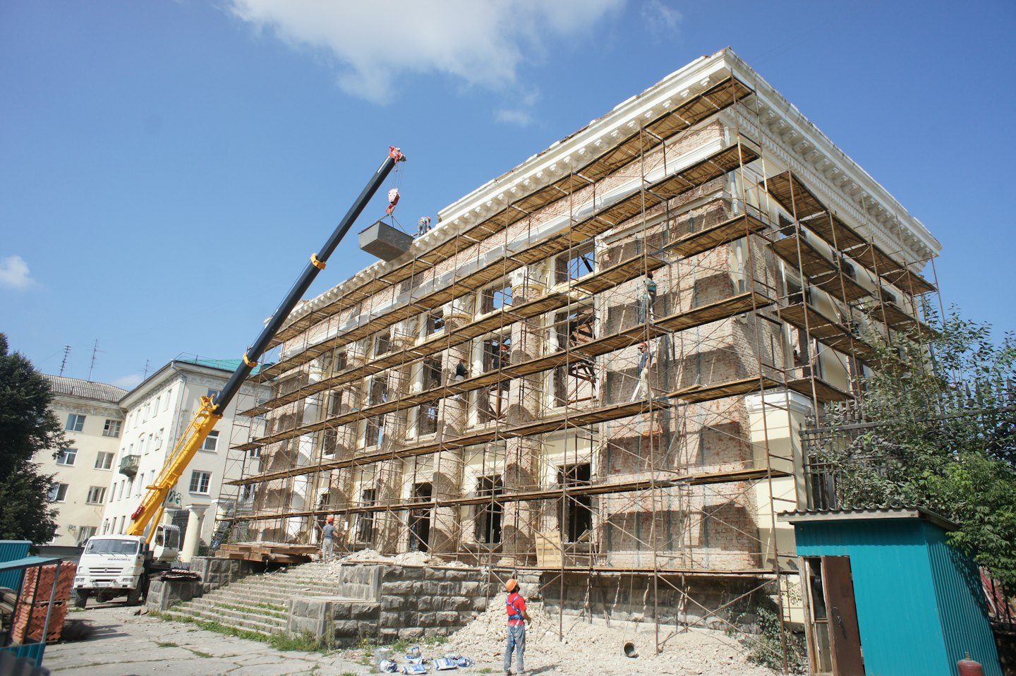 Bouwvakkers renoveren een bakstenen gebouw met steigers en een kraan.